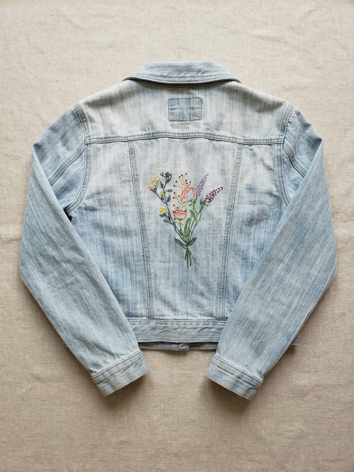 Light blue denim jacket with hand-embroidered wildflower bouquet on the back