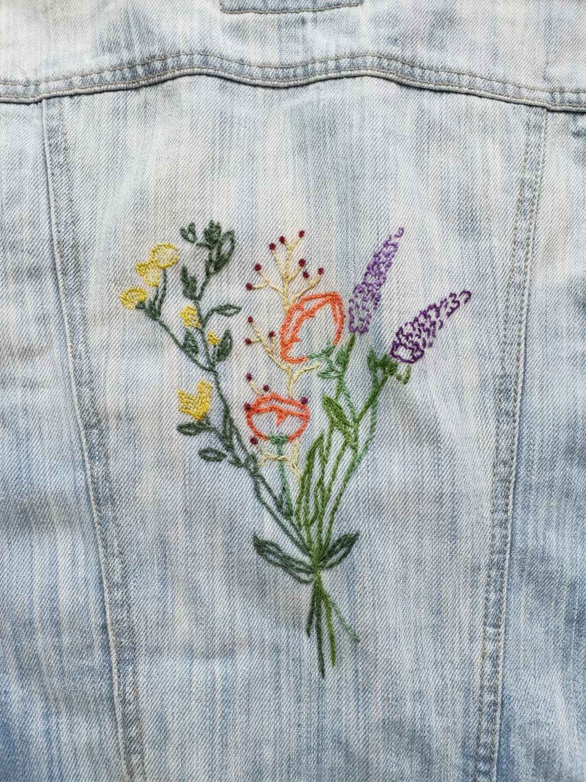 Close-up of embroidered wildflower bouquet with yellow, orange, and purple flowers on denim